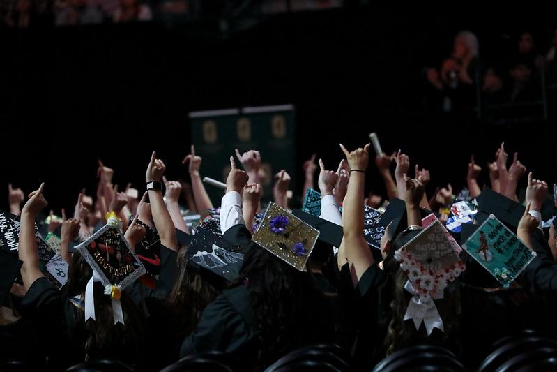 commencement graduates with caps on and stingers up fingers up